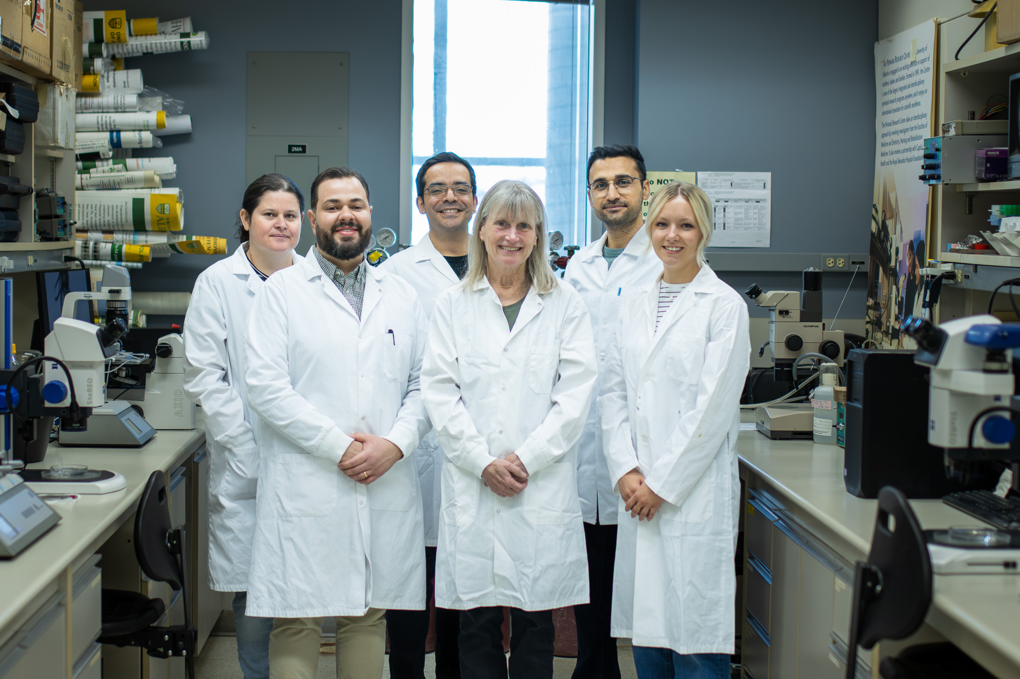 Six scientists wearing lab coats stand together in a medical research lab.